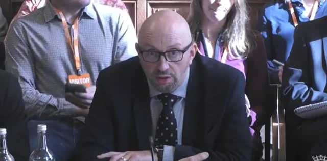 A bald man with black glasses wearing a suit.