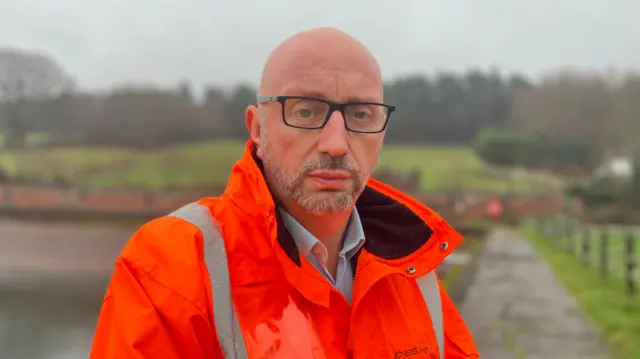 A bald man with glasses and an orange South East Water coat.