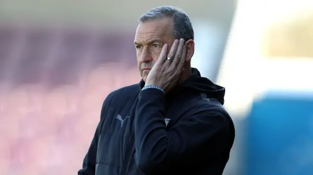 A photo of Colin Calderwood with his hand to his face wearing a wedding ring and a black PUMA jacket