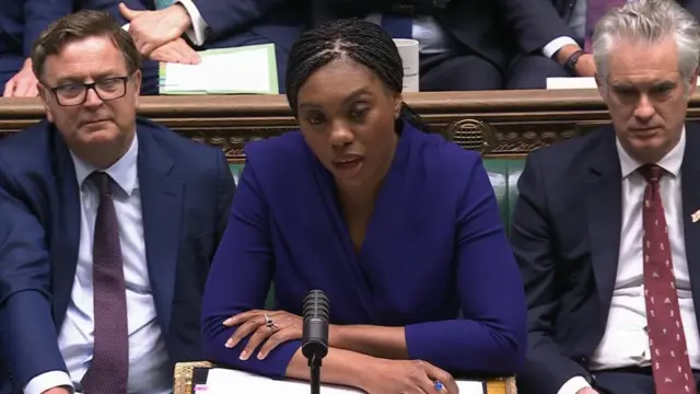 Kemi Badenoch in blue jacket speaking into microphone at parliamentary table