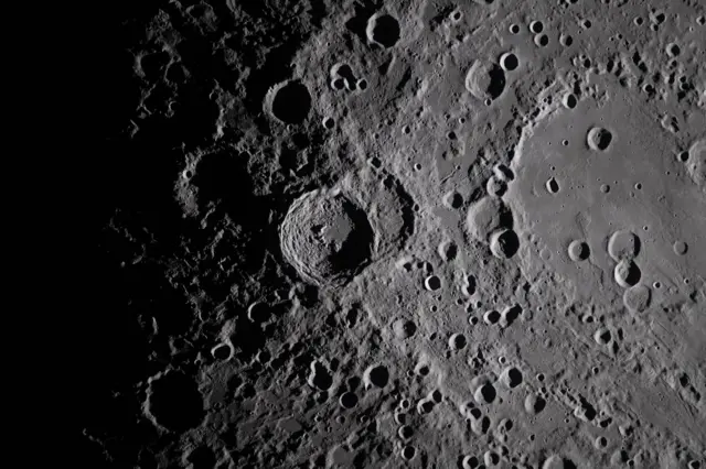 A close photo of a large crater on the surface of the Moon. It's surrounded by other, smaller craters.