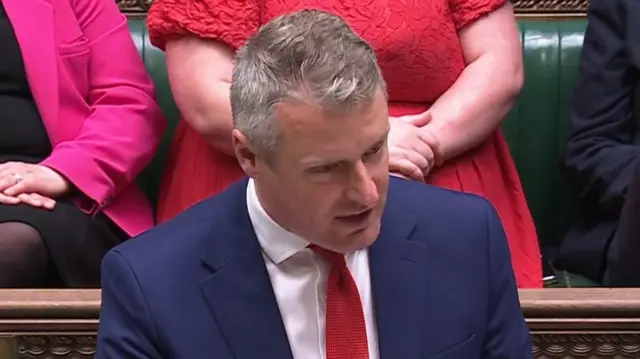 Luke Pollard in navy suit and red tie speaking at dispatch box in green parliamentary chamber