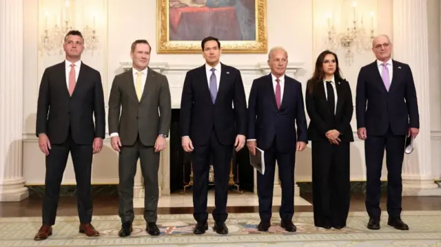 A row of six people stand inside a State Department building