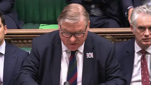 Mark Francois wearing glasses and dark suit speaks at dispatch box in green parliamentary chamber
