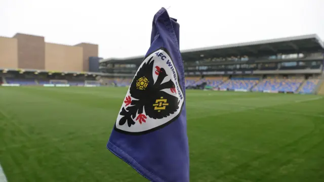 A photo of blue corner flag at the Cherry Red Records Stadium with the image of AFC Wimbledon's club crest