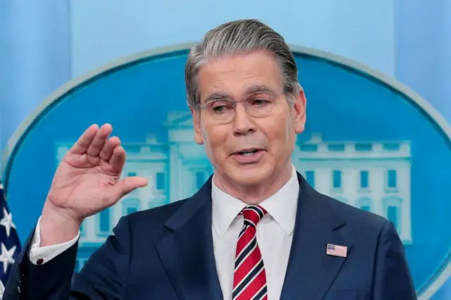 A man with grey hair and a red, white and blue striped tie wearing a blue suit