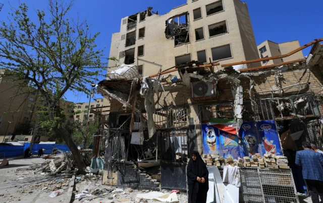 A woman stands next to debris lying in front of a residential building damaged by a strike