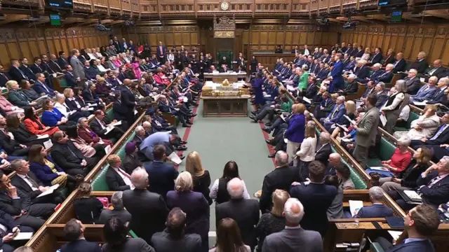 Wide view of a packed parliamentary chamber with members seated on green benches facing each other
