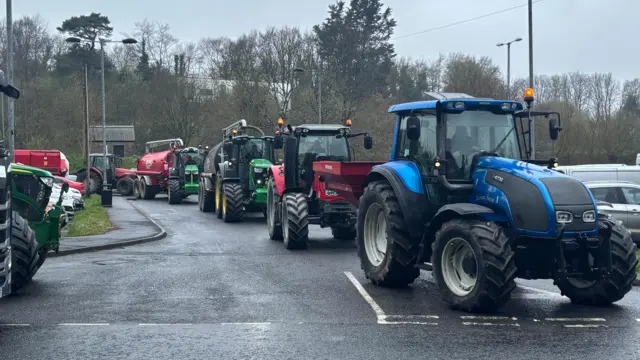 Numerous tractors slow traffic to a stop in Omagh, of colours blue red and green.
