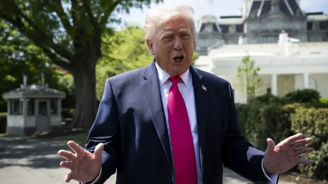 Donald Trump mid-speech as he addresses the media outside the White House wearing a dark blue suit, white shirt and red tie