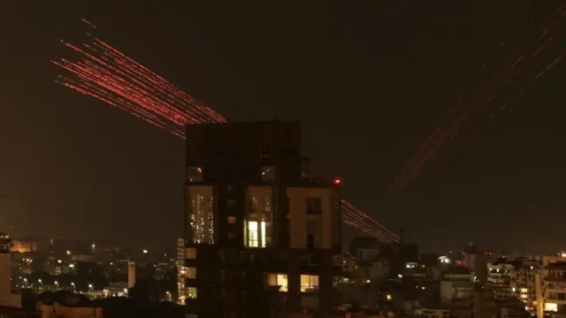 a city skyline at night with red firework-like streaks in the sky