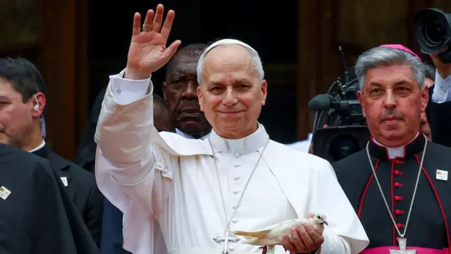 Pope Leo XIV waves as he holds a bird after a meeting for peace with the community of Bamenda