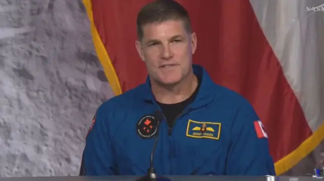 Jeremy Hanson speaking into a microphone, wearing a blue NASA outfit