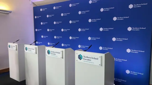 Four white podiums stand beside each other. They each have a sign that says 'Northern Ireland Executive'.