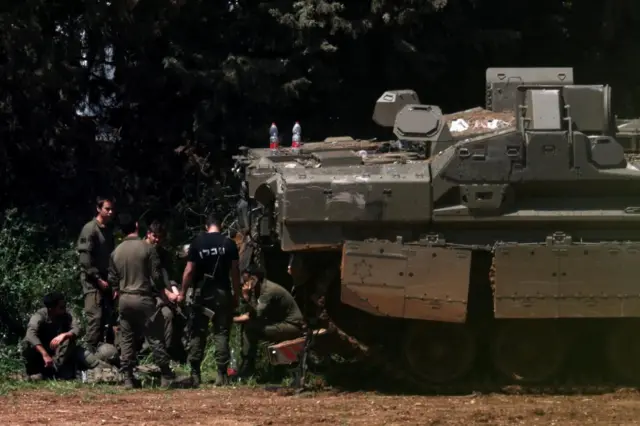 Israeli soldiers rest next to an armoured vehicle near the Israel-Lebanon border