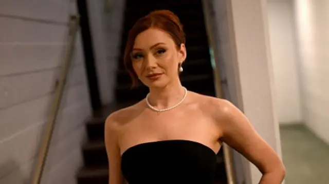 Elz the Witch wears a pearl necklace and a black dress as she steps down some stairs backstage at the Bafta Games Awards 2025