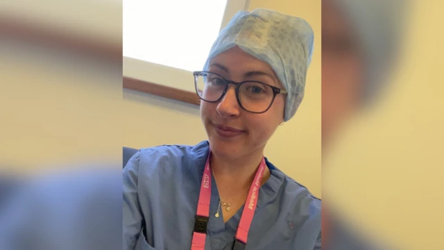 A young woman wearing scrubs smiles in front of the camera. She's wearing glasses and a hair cover
