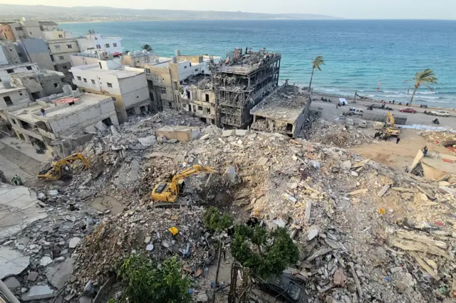 A crater of rubble is seen from the air with diggers operating next to residential buildings adjacent to the sea in Tyre, Lebanon