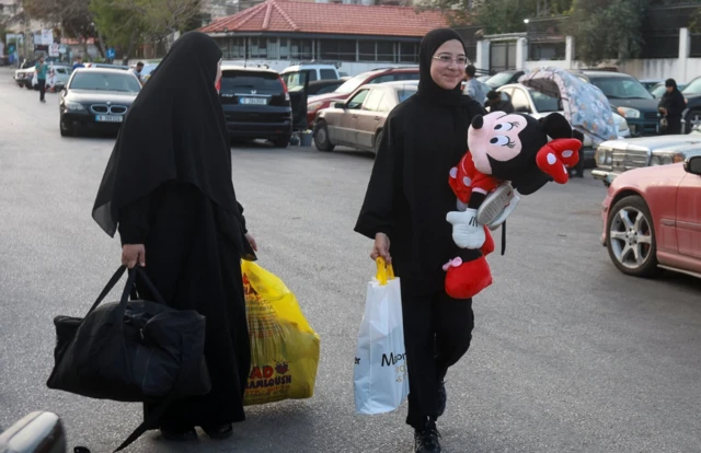 One girl clings onto a toy and a bag of belongings as she walks along a road