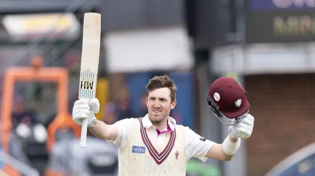 Somerset stand-in captain Craig Overton raising his bat and his helmet after scoring a century for his side.
