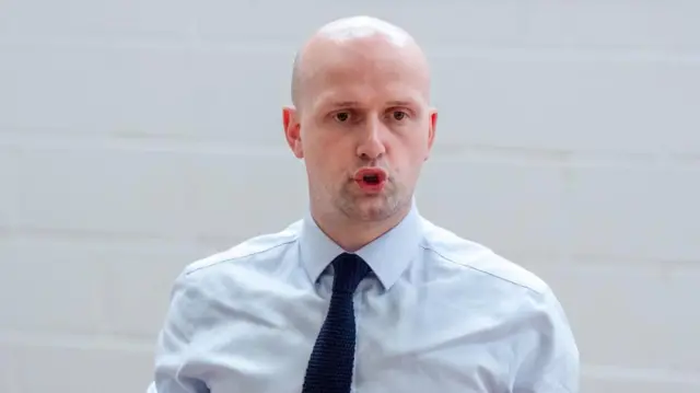 Head shot of Flynn who speaks with his mouth open in front of a white brick wall