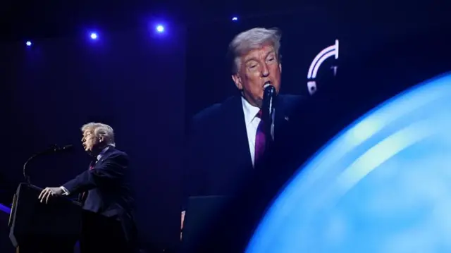 Donald Trump speaking into a microphone and projected on to a screen