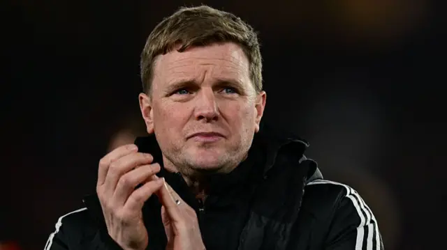 Newcastle manager Eddie Howe dressed in a black coat against a dark background. He is clapping his hands.