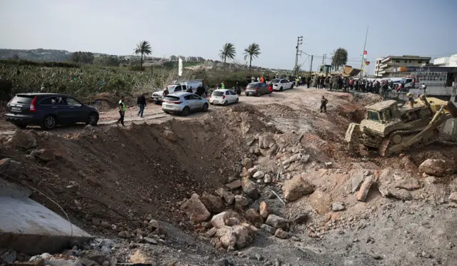 People cross a makeshift bridge in vehicles as crowds gather to oversee repairs to a bridge that was destroyed in an Israeli attack, in southern Lebanon on Friday.
