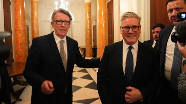 Mandelson and Starmer stand in a tiled corridor