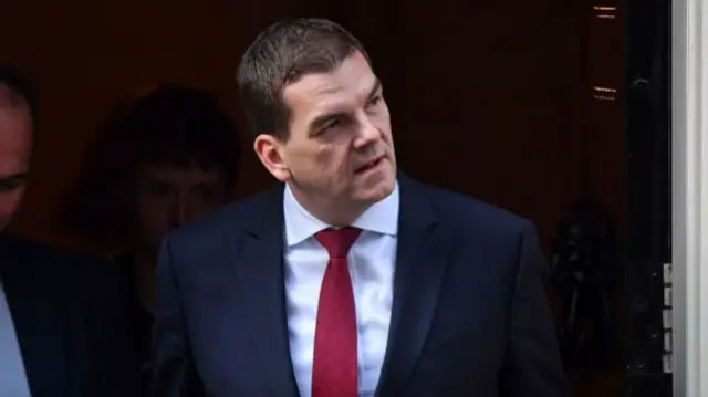 Olly Robbins walks out of No 10 Downing Street. He wears a dark blue suit jacket, a white shirt and red tie.