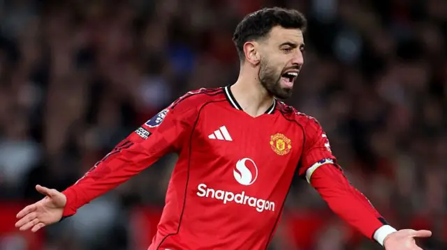 Bruno Fernandez celebrates with his arms outstretched in a red Man United kit