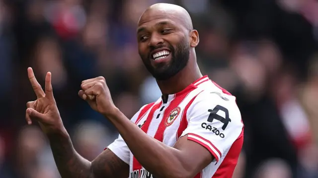 Iago Thiago mimicking two nil with his hands, he's in a red and white striped jersey and is smiling