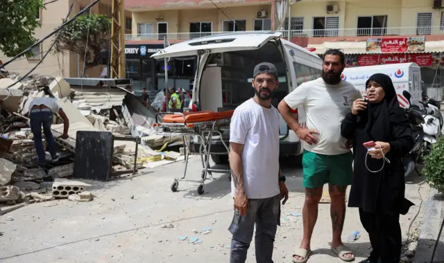 People stand in front of an ambulance with a stretcher loaded into it next to people clearing rubble in Tyre on Friday.