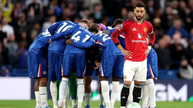 The Chelsea team huddle as Bruno Fernandes of Manchester United looks on prior to kick off