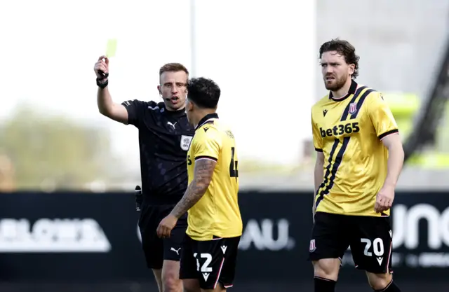 Referee Adam Herczeg (left) shows Stoke City's Million Manhoef (centre) a yellow card