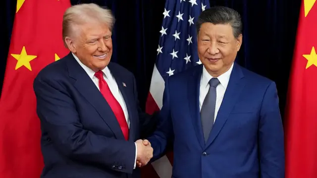 US President Donald Trump and Chinese President Xi Jinping shake hands as they stand in front of US and Chinese flags at Gimhae Air Base on October 30, 2025 in Busan, South Korea.