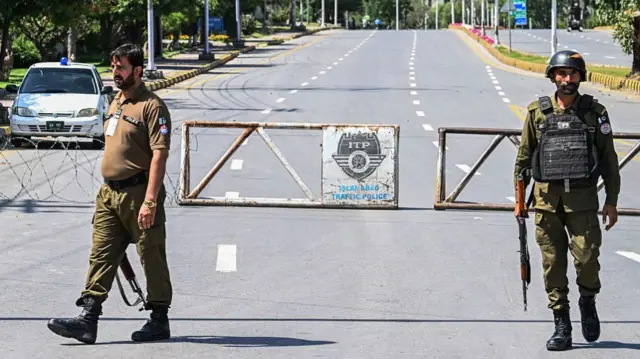 Two armed guards stand in front of barrier and razor wire on empty road