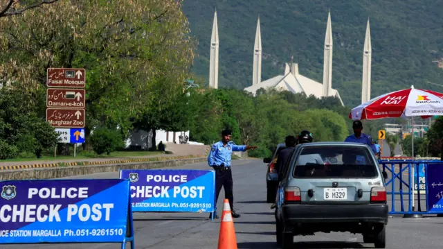 A policeman signals to a blue car approaching a police checkpoint