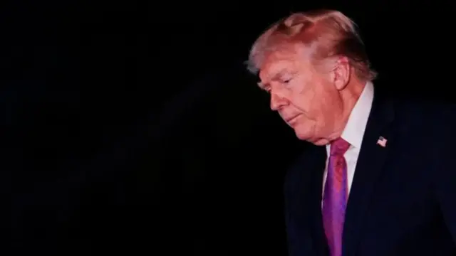 Ο Ντόναλντ Τραμπ κοιτάζει ψηλά σε μαύρο φόντο, φορώντας ένα κοστούμι με έντονο μωβ γραβάτα