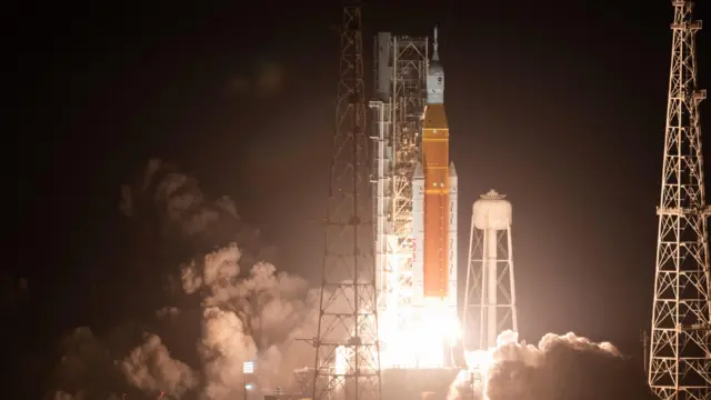 Artemis one blasts off - fire burns below the orange rocket as it takes off