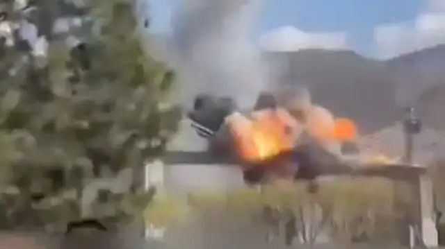 A large fireball erupts on the span of a bridge, mountains are in the background