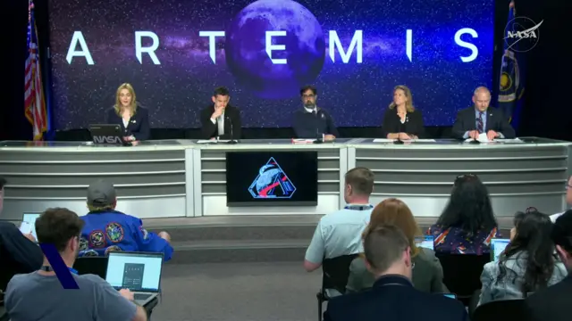 Line of four people sitting behind table with a screen with the word 'Artemis' on it behind them