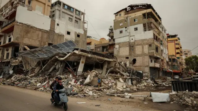 Two men on a scooter drive past a building that has been reduced to rubble by an Israeli strike in Tyre, Lebanon