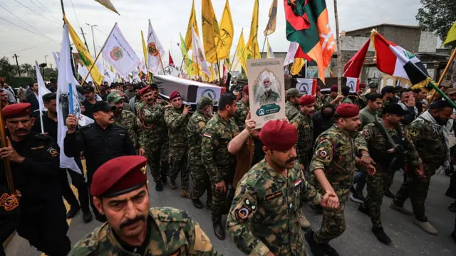 men in camo uniforms carry coffins through a street while flying flags