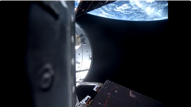 A picture showing a black sky, the Earth visible partially in the background. Part of the spacecraft including a solar array can be seen on the left of the picture