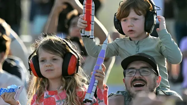 Children with ear defenders and toy rockets watch the launch of Artemis II in Cape Canaveral, Florida