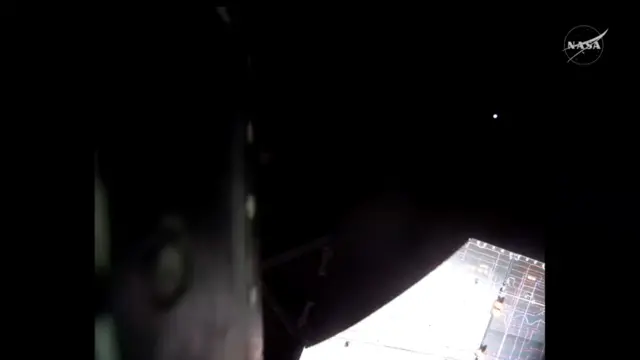 View from the outside of the Orion capsule where a distant Moon can be seen on the top right of the screen