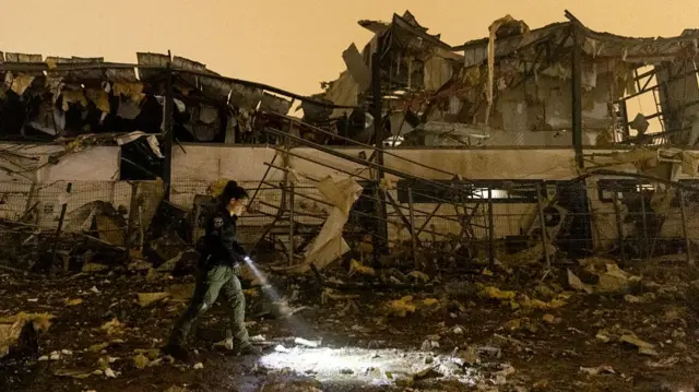 worker holding flashlight while walking through rubble of destroyed building