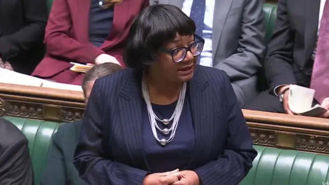 Diane Abbott speaks in Parliament, wearing a blue pinstripe jacket.