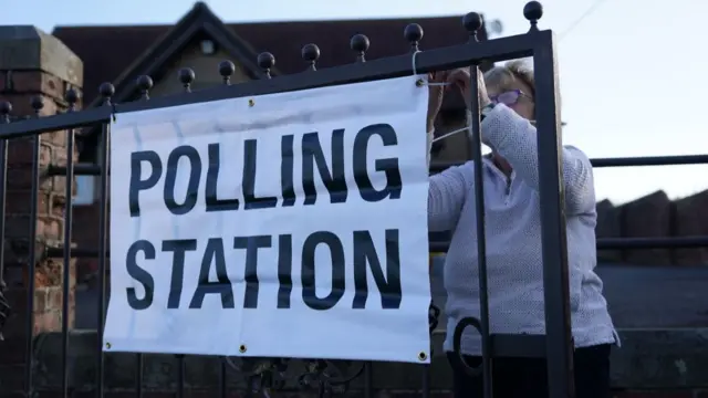 A woman prepares a banner hanging on a gate at a polling station